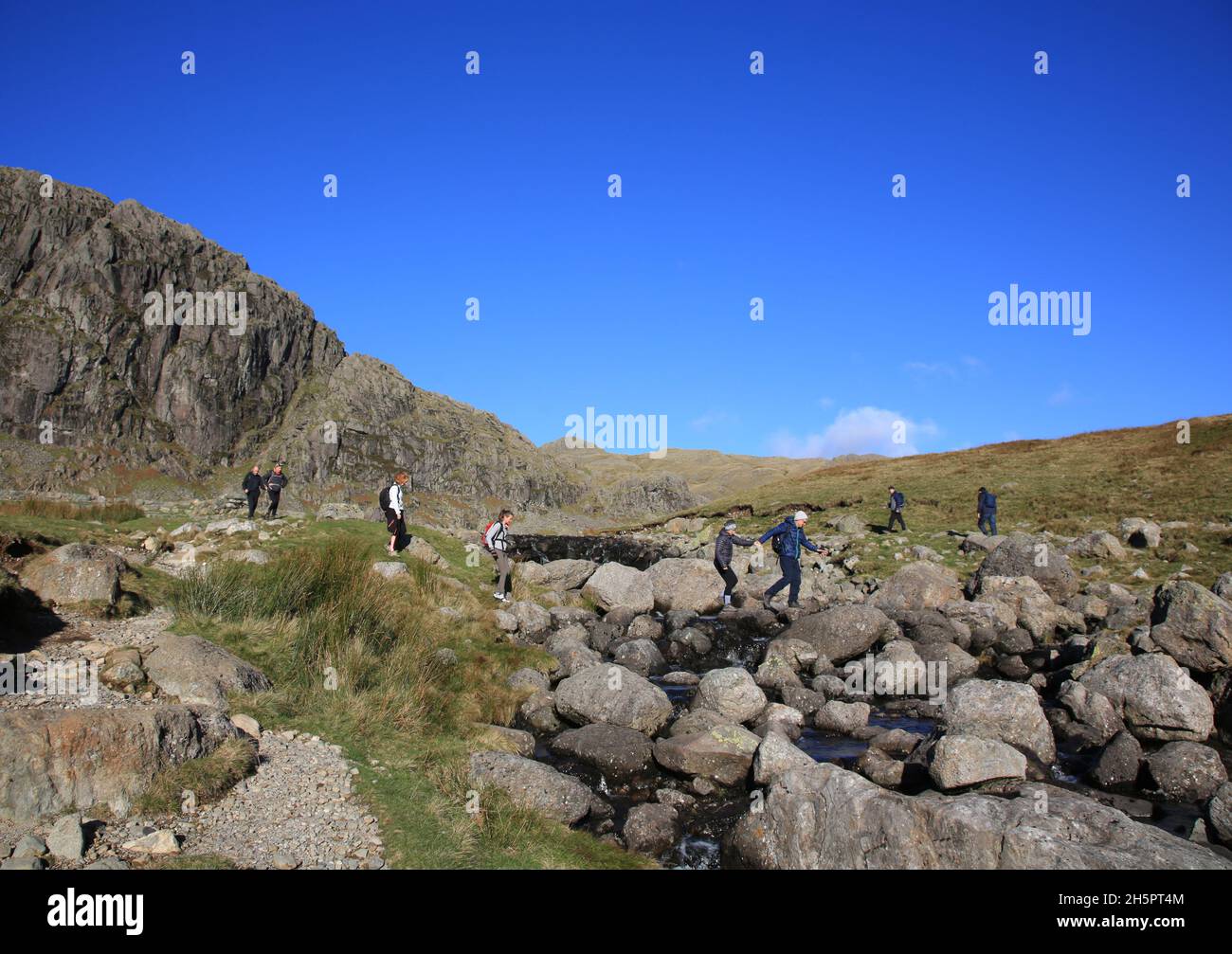 Wanderer, die Stickle Ghyll im Lake District Nationalpark, Cumbria, England, Großbritannien, überqueren. Stockfoto