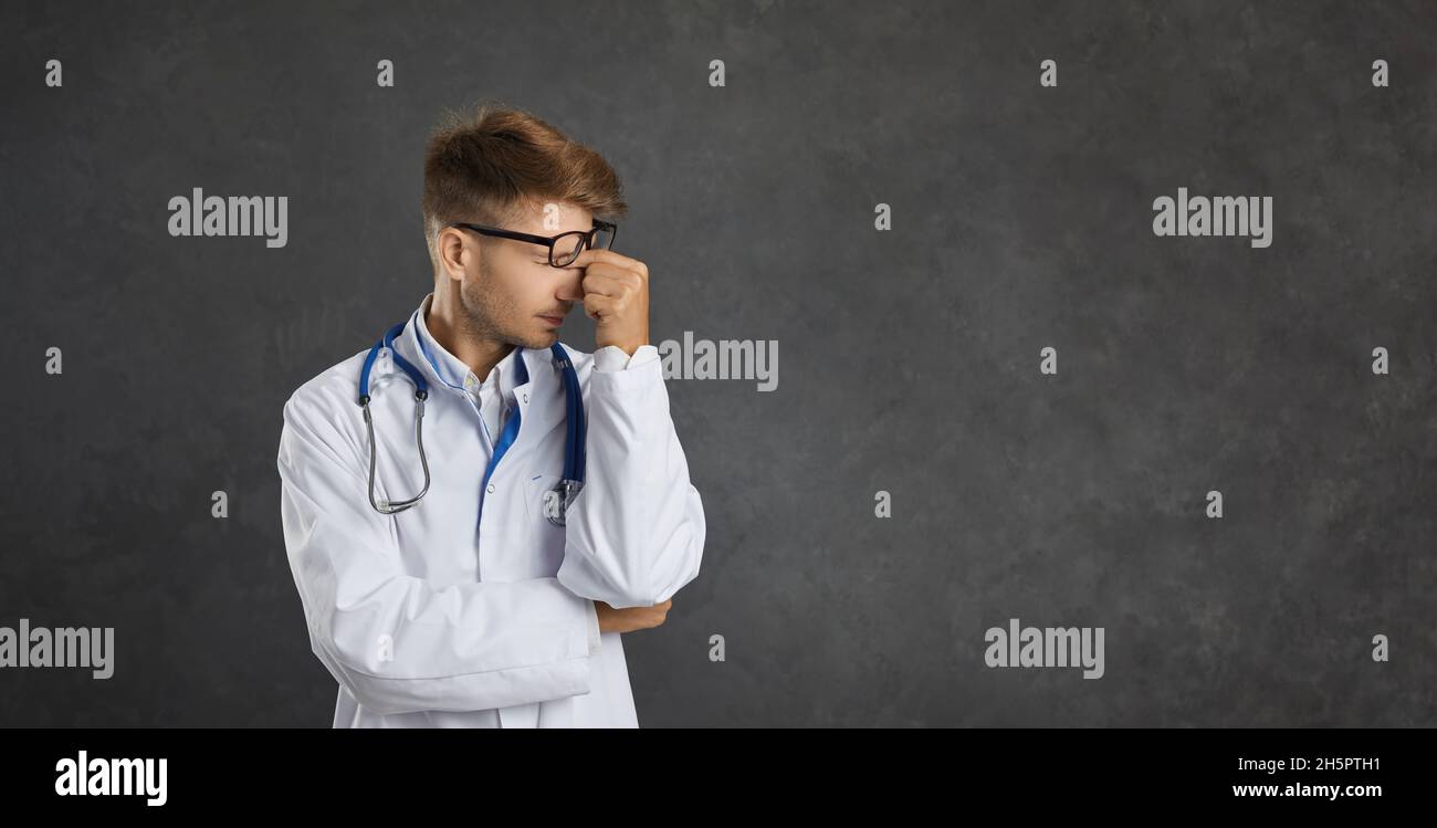 Porträt eines jungen erschöpften männlichen Arztes, der auf dem Hintergrund einer grauen Betonwand steht. Stockfoto