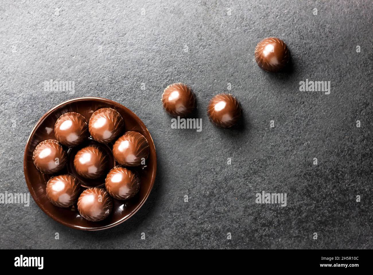 Schokoladen-Bonbons auf einem Teller auf schwarzem Hintergrund mit Platz zum Kopieren. Flach liegend, Draufsicht Stockfoto