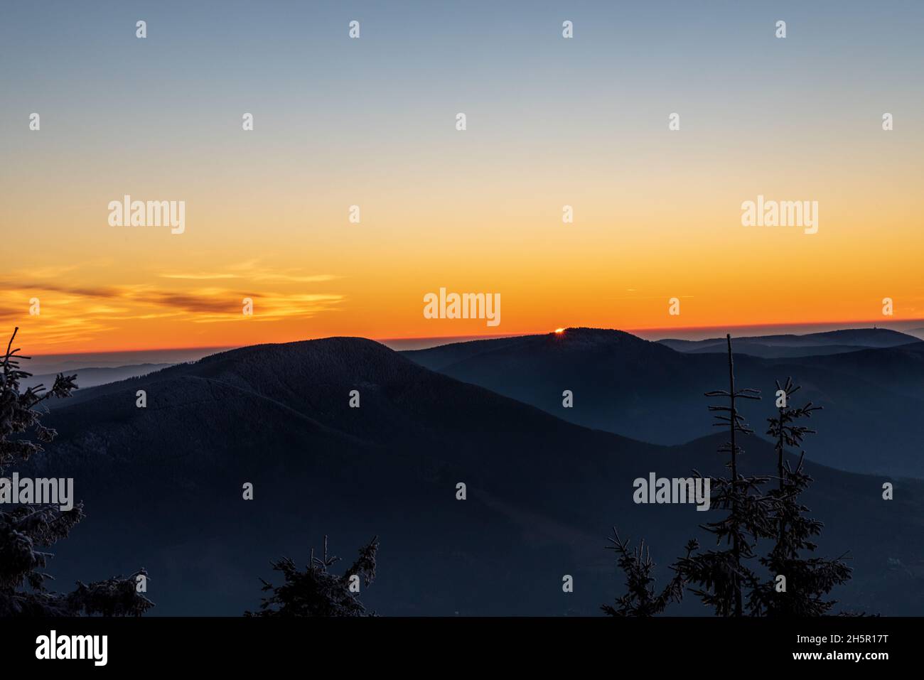 Sonnenuntergang mit orangefarbenem Himmel und wenigen Wolken vom Lysa hora-Hügel in den Moravskoslezske Beskydy-Bergen in Tschechien Stockfoto