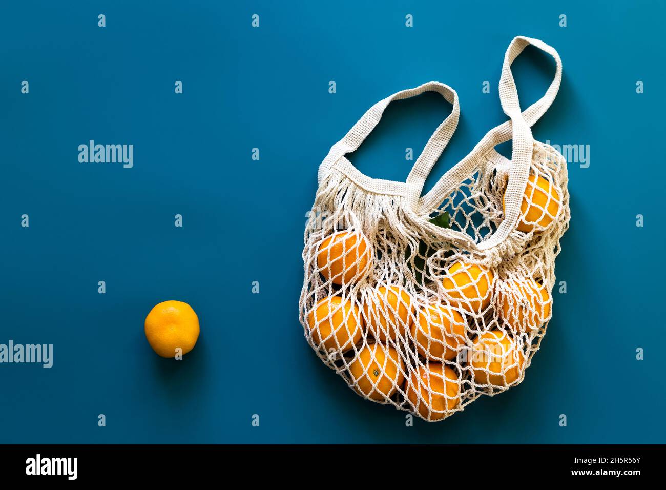 Mandarinen oder Mandarinen Früchte in Baumwolle umweltfreundliche Netztasche auf blauem Hintergrund. Konzept von Zero Waste, plastikfreiem Einkaufen oder Öko-Food. Draufsicht. Stockfoto