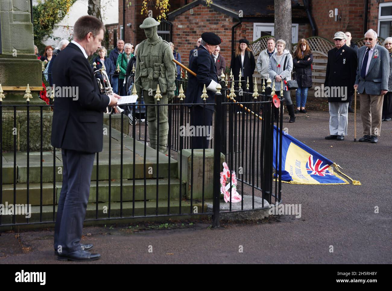 Syston, Leicestershire, Großbritannien. November 2021. Der Standard wird während der gedenkfeiern zum Waffenstillstandstag im Syston war Memorial in der Nähe eines lebensgroßen gestrickten Soldaten gesenkt. Credit Darren Staples/Alamy Live News. Stockfoto