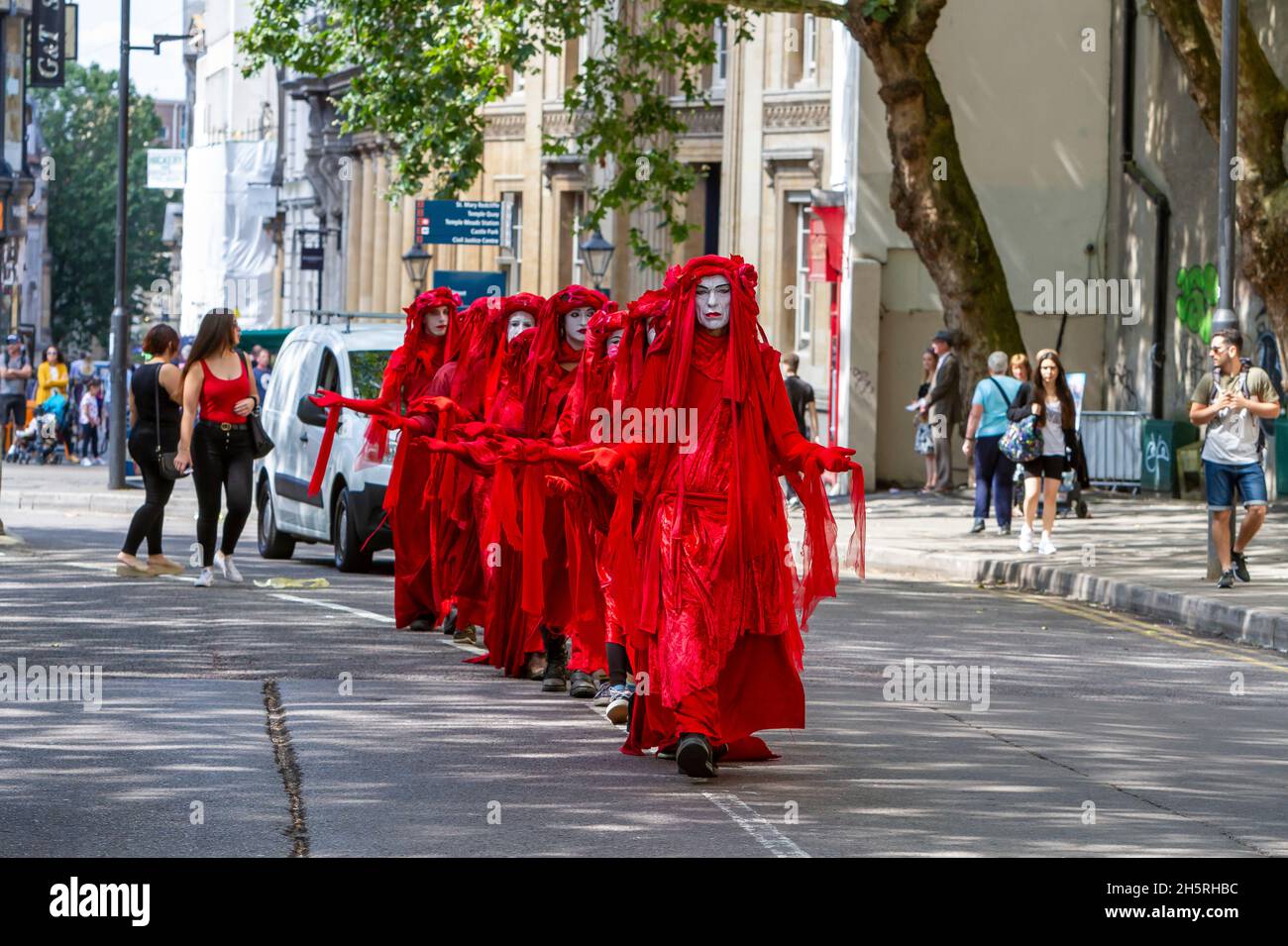 Straßenfoto einer Gruppe von Darstellern des „Invisible Circus“ der Roten Brigade, die eine Demonstration zum Klimawandel durch die Straßen einer Stadt führen. Stockfoto