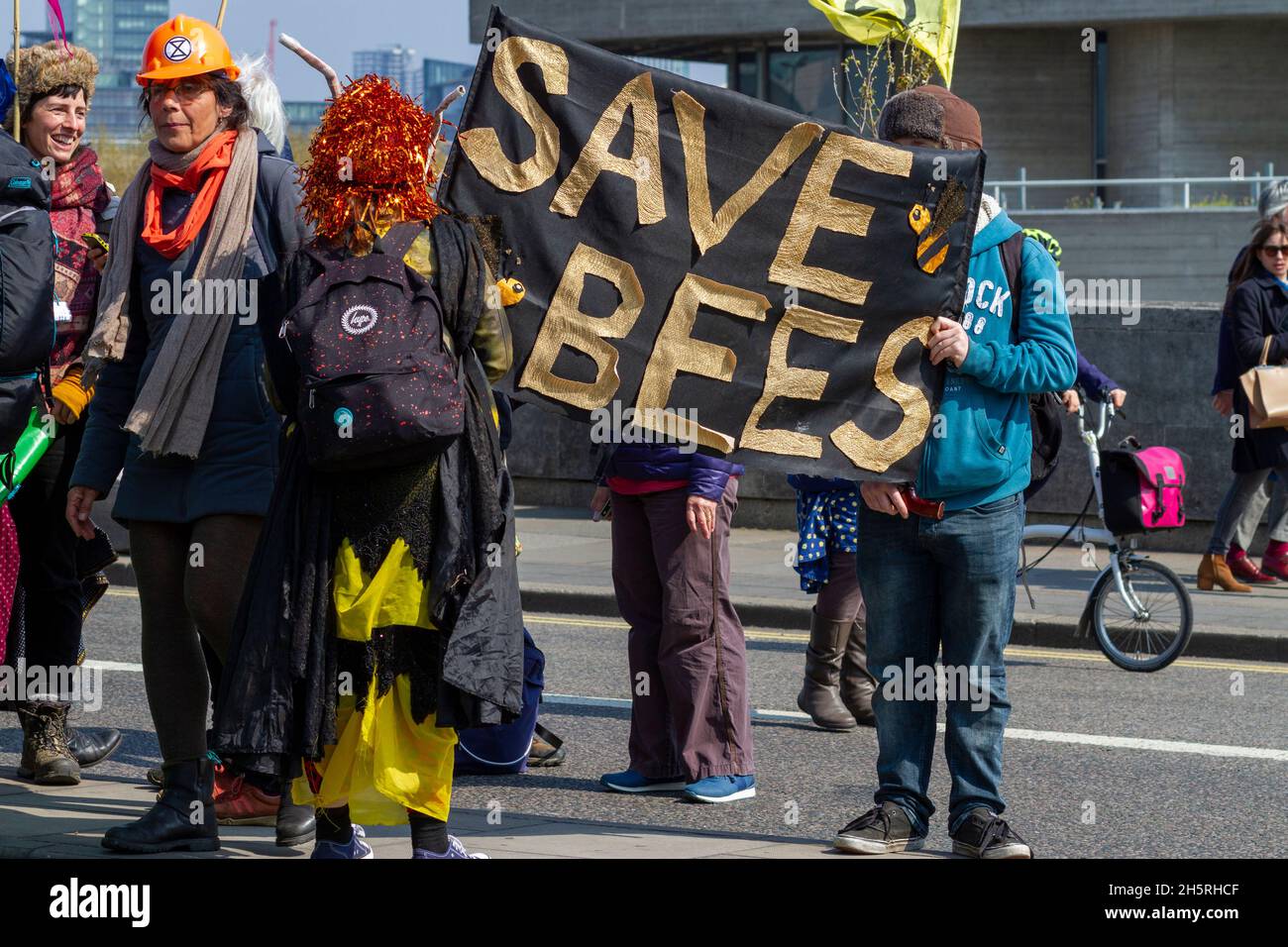 Straßenfoto von Demonstranten bei einer Klima-Notstandsskundgebung mit einem großen Transparent „Rette die Bienen“ und in Kostüm. Banner ist Mittelbild Stockfoto