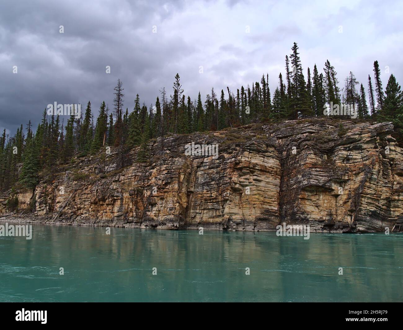Blick auf die farbenfrohe, erodierte Felswand mit sichtbaren Schichten am Athabasca River im Jasper National Park, Alberta, Kanada, in den Rocky Mountains mit Bäumen. Stockfoto