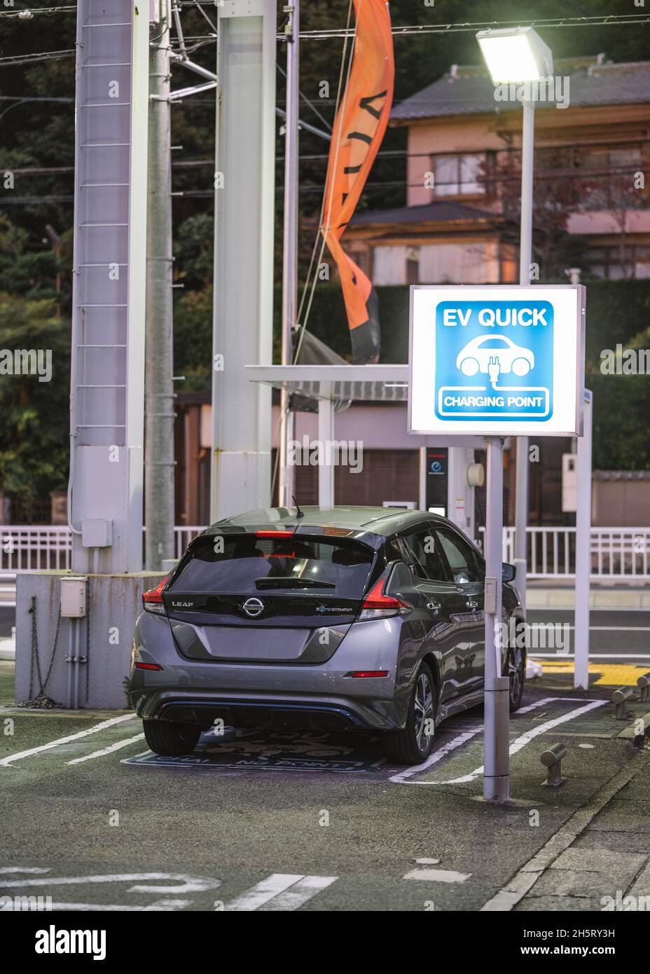 Nissan Leaf wird an der EV Quick-Ladestelle für Elektrofahrzeuge geladen. Blaues Leuchtzeichen. Stockfoto