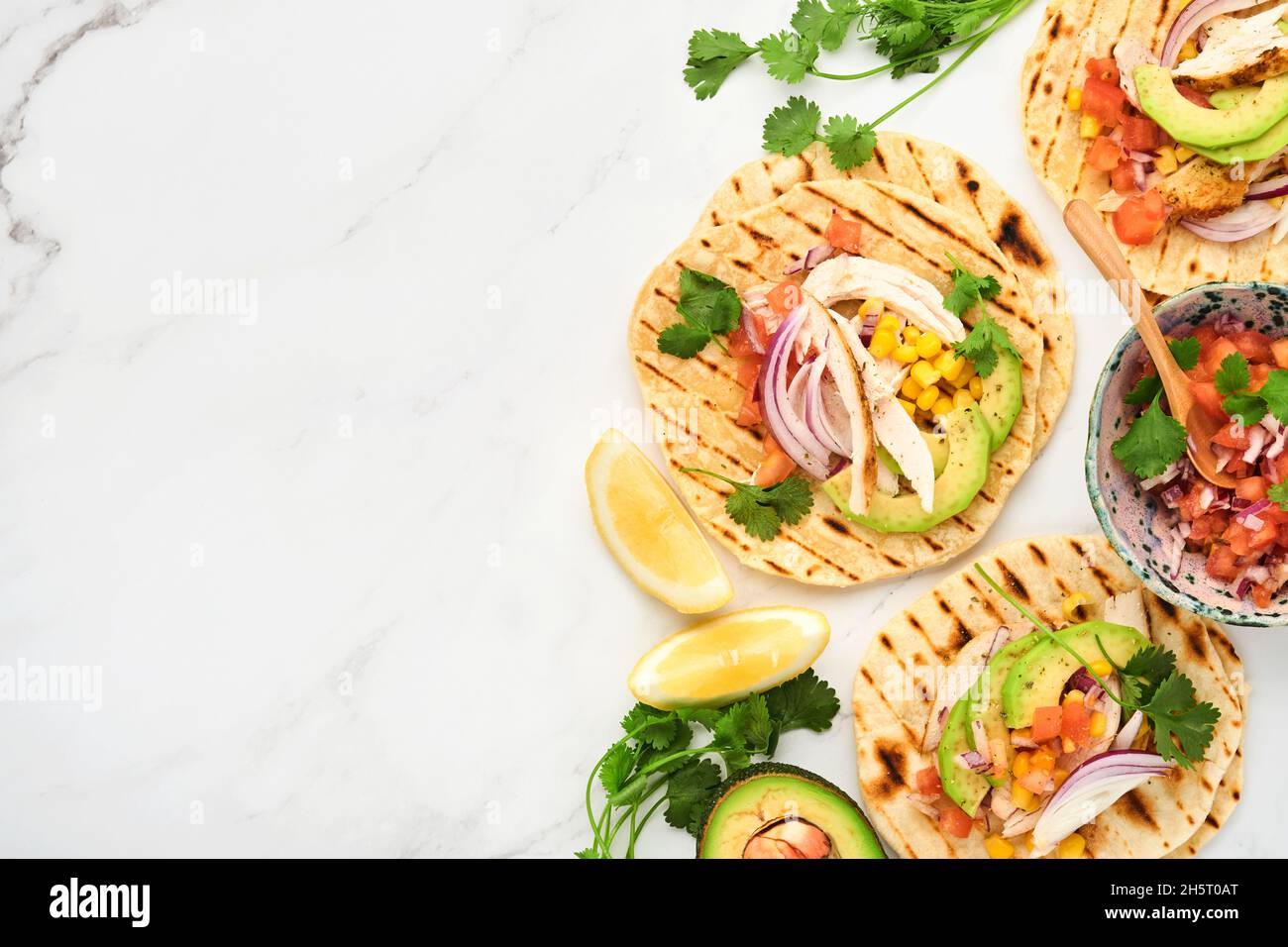 Mexikanische Tacos mit gegrilltem Hähnchen, Avocado, Maiskörnern, Tomaten, Zwiebeln, Koriander und Salsa am Tisch aus weißem Stein. Traditionell mexikanisch und lateinamerikanisch Stockfoto