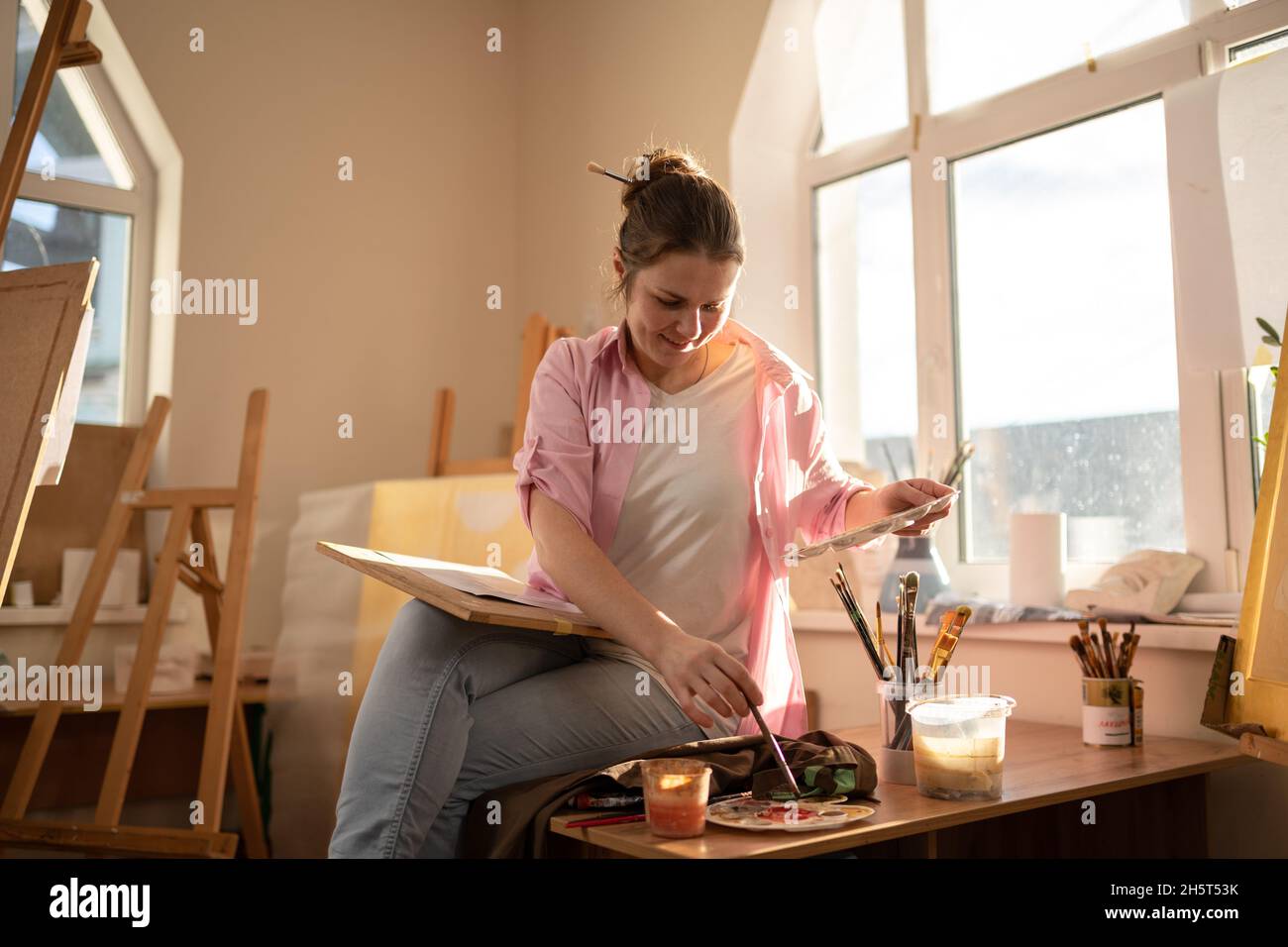 Nette Frau malt in einer Kunstwerkstatt auf Leinwand. Künstler, der ein Bild erstellt. Kunstschule oder Atelier. Arbeiten Sie mit Farben, Pinsel und Staffelei. Hobby und Freizeit Stockfoto