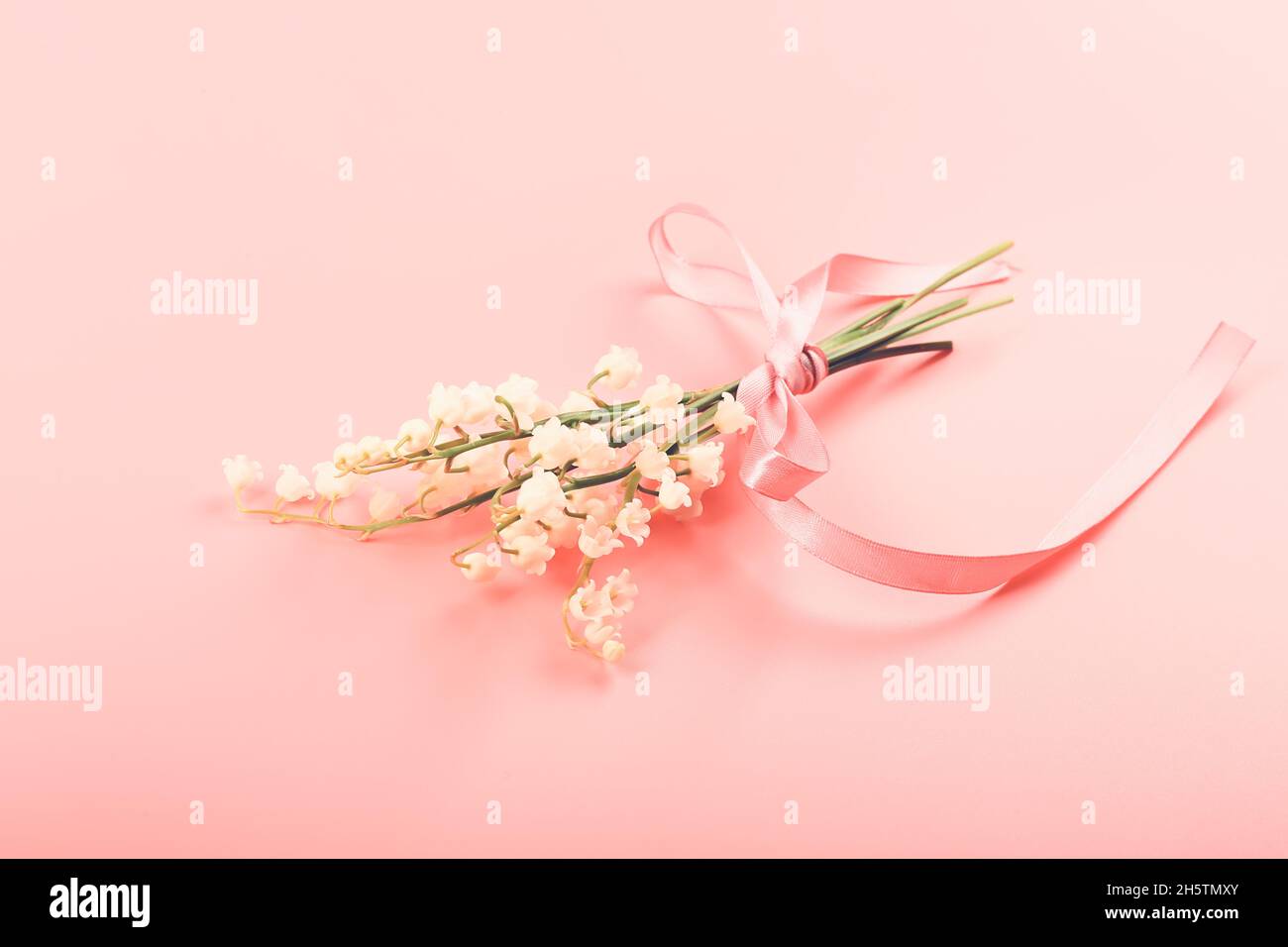 Maiglöckchen, gebunden mit einem rosa Band auf einem rosa Hintergrund. Zartes Federkonzept Stockfoto