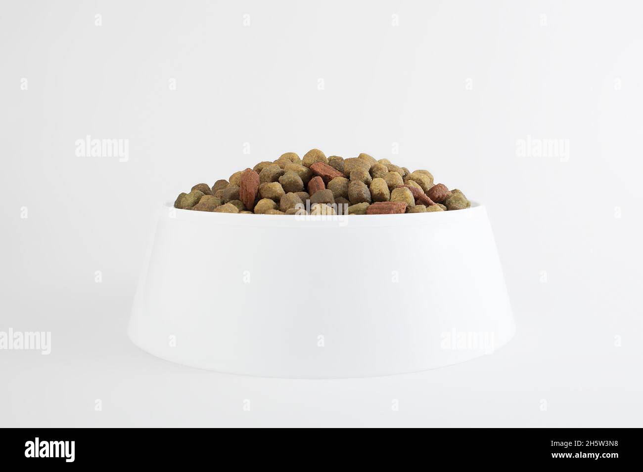 Futter für einen Hund oder eine Katze. Trockenfutter für Jungtiere oder Welpen aus nächster Nähe in einer weißen Schüssel auf weißem Hintergrund. Konzept - Werbung für Trockenfutter für Haustiere. Cop Stockfoto