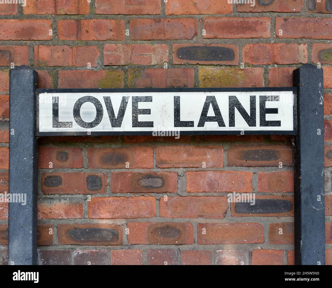 Nahaufnahme des Straßenschildes mit der Aufschrift „Love Lane“ an einer roten Backsteinmauer in einer Stadt Stockfoto