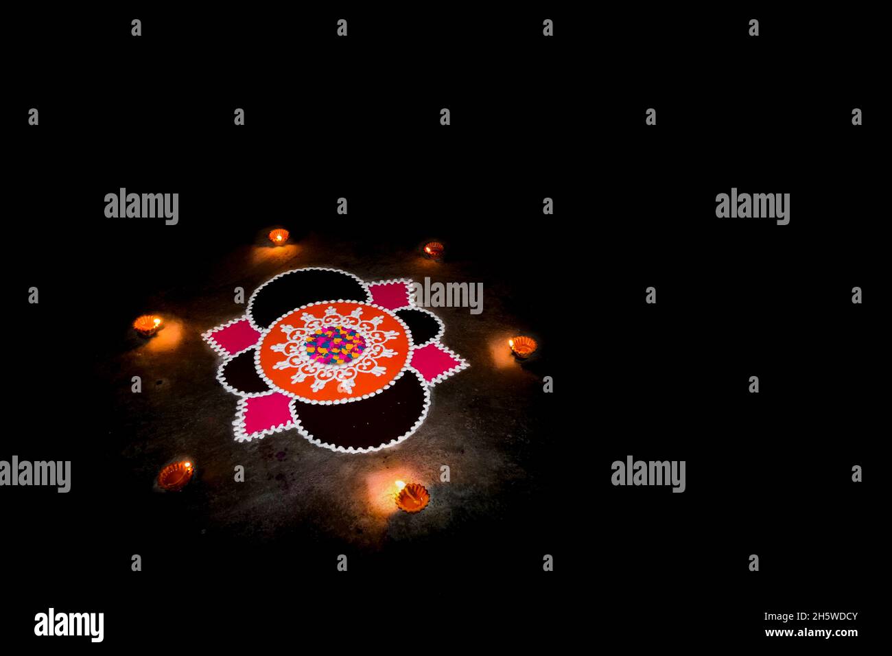 Rangoli vor der Tür des Hauses in der Abendzeit mit diwali diya um sie während des Festivals des Lichts diwali in Indien. Schwarzer Hintergrund Stockfoto