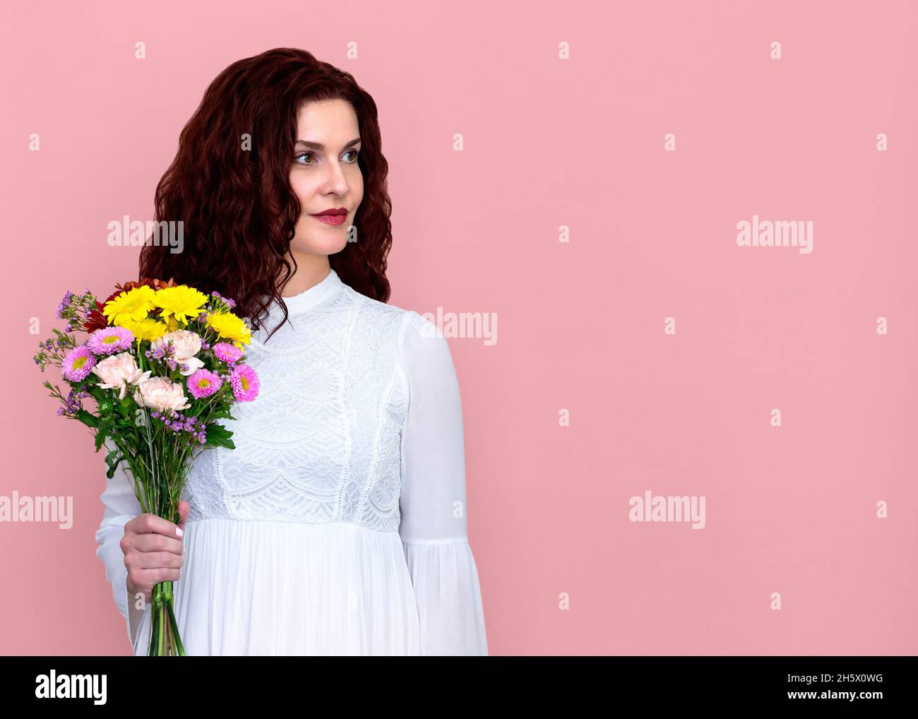 Frau hält Blumenstrauß Blick nach links auf rosa Hintergrund. Porträt einer hübschen Frau mit Blumenstrauß in einer Hand. Stockfoto