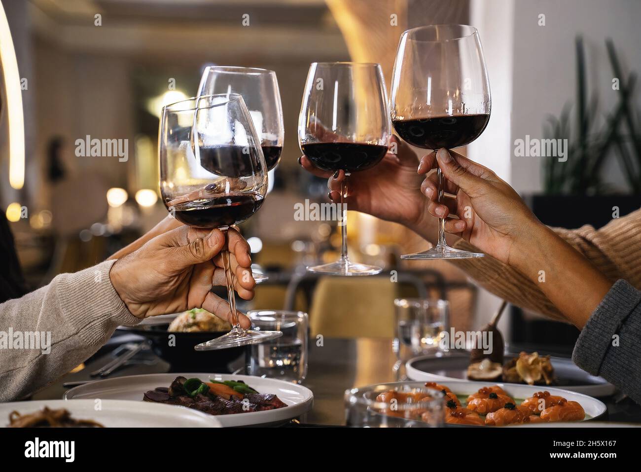 Nahaufnahme der Hände mit Gläsern beim Toasten von Rotwein im Restaurant - eine Gruppe von Freunden feiern klirrende Weingläser Stockfoto
