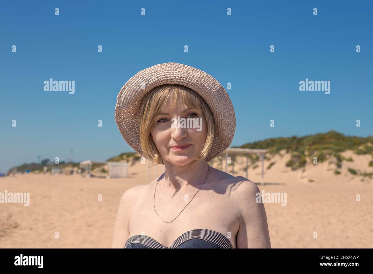 Porträt einer reifen Frau in Hut und Bikini am Strand an einem sonnigen Sommertag. Stockfoto
