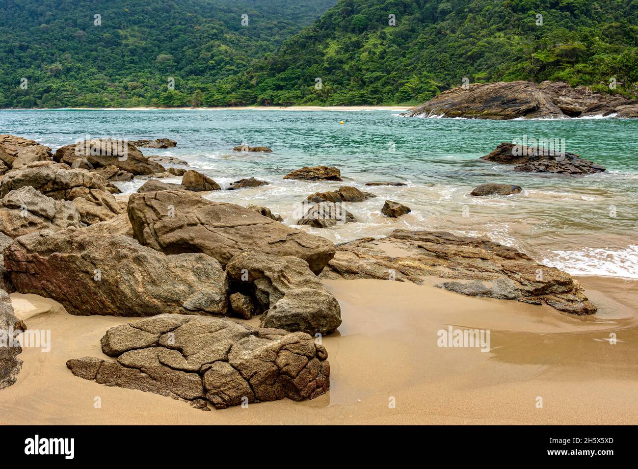 Felsiger und einsamer Strand, umgeben von dichtem und erhaltenem Regenwald mit ruhigem Wasser und lebendigen Farben in Trindade, Paraty, Rio de Janeiro Stockfoto
