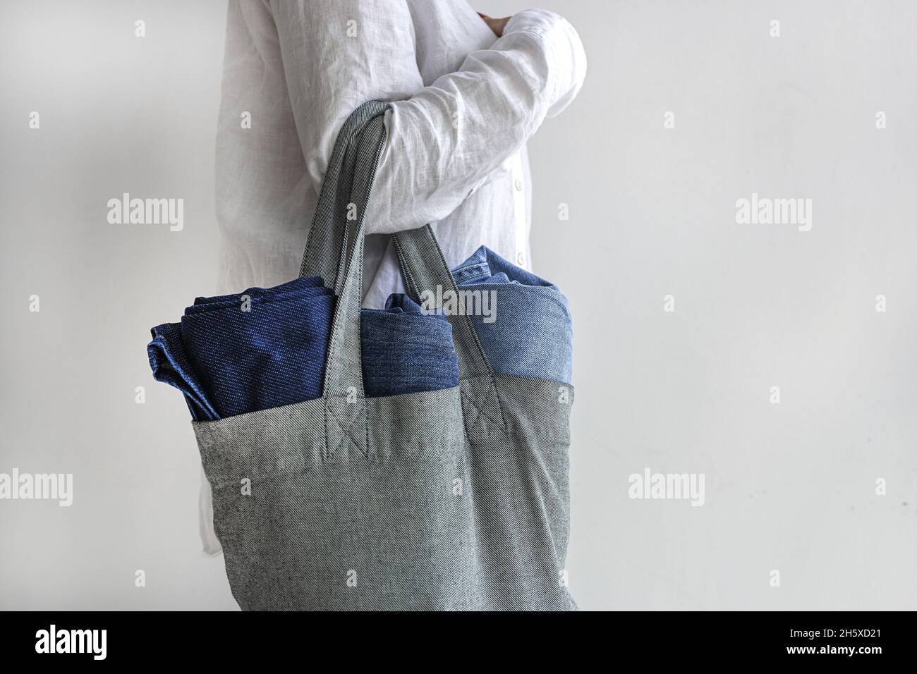 Seitenansicht einer anonymen Shopper-Frau mit schwerer wiederverwendbarer Einkaufstasche und Denim-Jeans Stockfoto