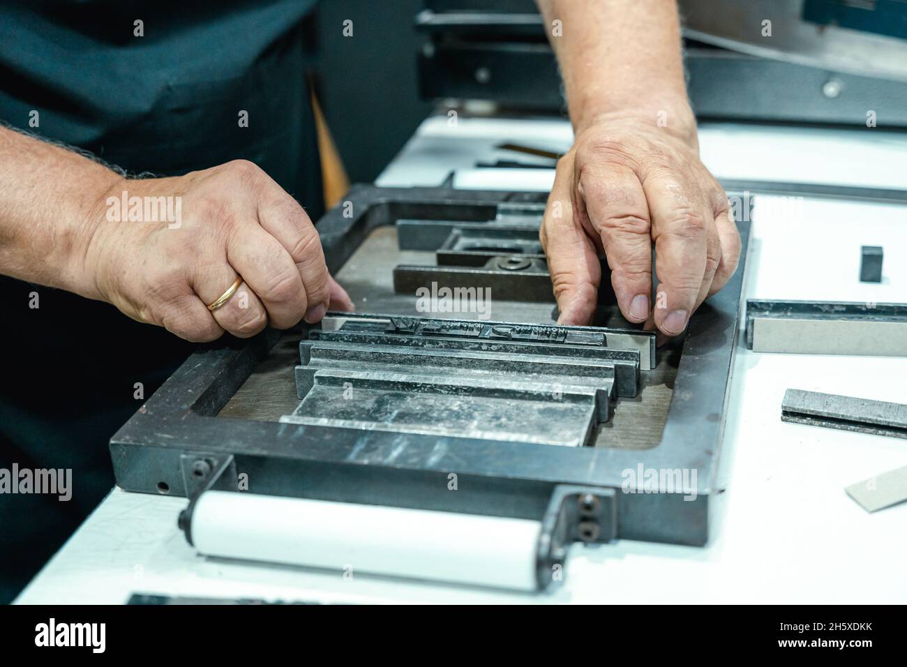 Hoher Erntewinkel unkenntlich älterer männlicher Handwerker in Schürze und Brille, der Metallrahmen für den Buchdruck im Studio vorbereitet Stockfoto