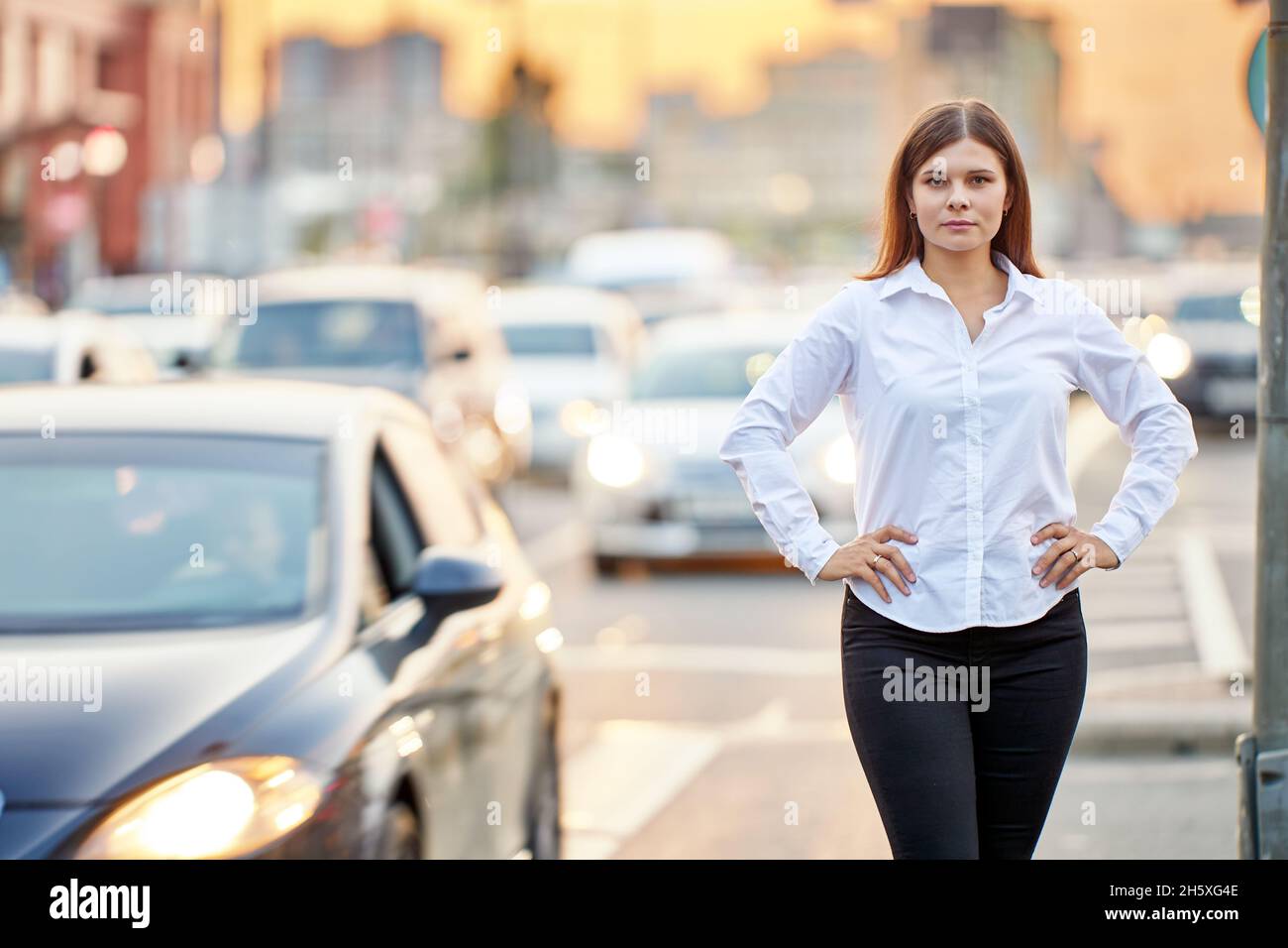 Viel Verkehr im Zentrum der Großstadt am Abend steht eine junge Frau auf der Straße mit ihren Händen auf den Hüften. Stockfoto