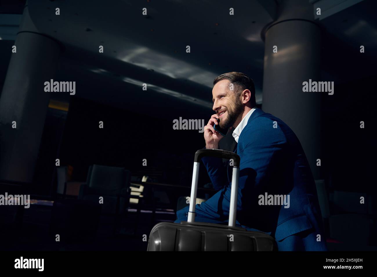 Ein gutaussehender europäischer Geschäftsmann spricht auf einem Sessel in der Hotellounge mit einem Mobiltelefon und lächelt zur Seite. Erfolgreicher Anlageberater mit Stockfoto