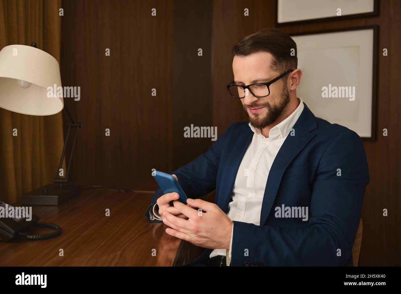 Schöner attraktiver erfolgreicher erfolgreicher Geschäftsmann, Geschäftsreisender, Investor mit Brillen, Lächeln und einem Mobiltelefon, das an einem Tisch sitzt Stockfoto