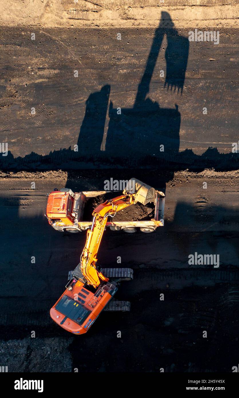 Leipzig, Deutschland. November 2021. 11. November 2021, Sachsen, Rötha: Ein Bagger und ein LKW werfen Schatten auf der Baustelle für die zukünftige A72 bei Rötha. Auch der letzte Bauabschnitt 5.2 ist der komplizierteste von allen. Fast die gesamte Strecke verläuft auf dem Gelände einer ehemaligen Tagebaumine und muss zuvor ausgiebig verdichtet werden. Bisher wurden fast 2 Millionen Kubikmeter Erde bewegt und gut 14,000 dieser Betonblöcke, die sogenannten Legosteine, wurden aufgestellt. (Luftaufnahme mit Drohne) Foto: Jan Woitas/dpa-Zentralbild/dpa Quelle: dpa picture Alliance/Alamy Live Ne Stockfoto