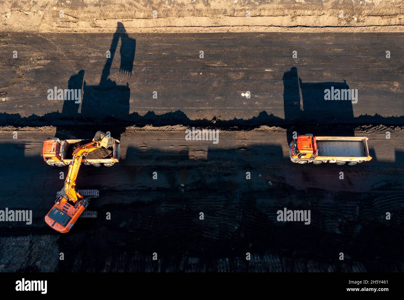 Leipzig, Deutschland. November 2021. 11. November 2021, Sachsen, Rötha: Ein Bagger und zwei Lastwagen werfen Schatten auf die Baustelle für die zukünftige A72 bei Rötha. Auch der letzte Bauabschnitt 5.2 ist der komplizierteste von allen. Fast die gesamte Strecke verläuft auf dem Gelände einer ehemaligen Tagebaumine und muss zuvor ausgiebig verdichtet werden. Bisher wurden fast 2 Millionen Kubikmeter Erde bewegt und gut 14,000 dieser Betonblöcke, die sogenannten Legosteine, wurden aufgestellt. (Luftaufnahme mit Drohne) Foto: Jan Woitas/dpa-Zentralbild/dpa Quelle: dpa picture Alliance/Alamy Live Stockfoto