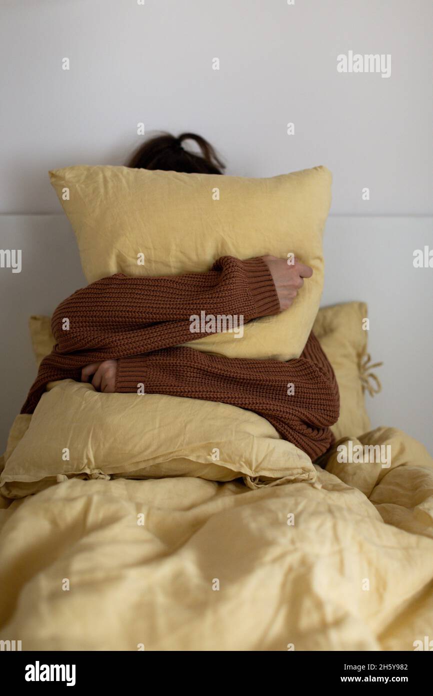 Das Mädchen umarmt ein gelbes Kissen, das in einem warmen Pullover im Bett sitzt. Das Konzept von Herbst und Winter. Stockfoto