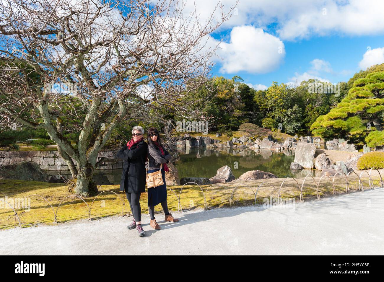 Zwei weibliche Touristen, die sich auf dem Weg, der an einem der wunderschönen, architektonisch gestalteten Gärten des Nijo Castle, Kyoto, Japan, vorbeiführt, zurück in die Vergangenheit stellen. Stockfoto