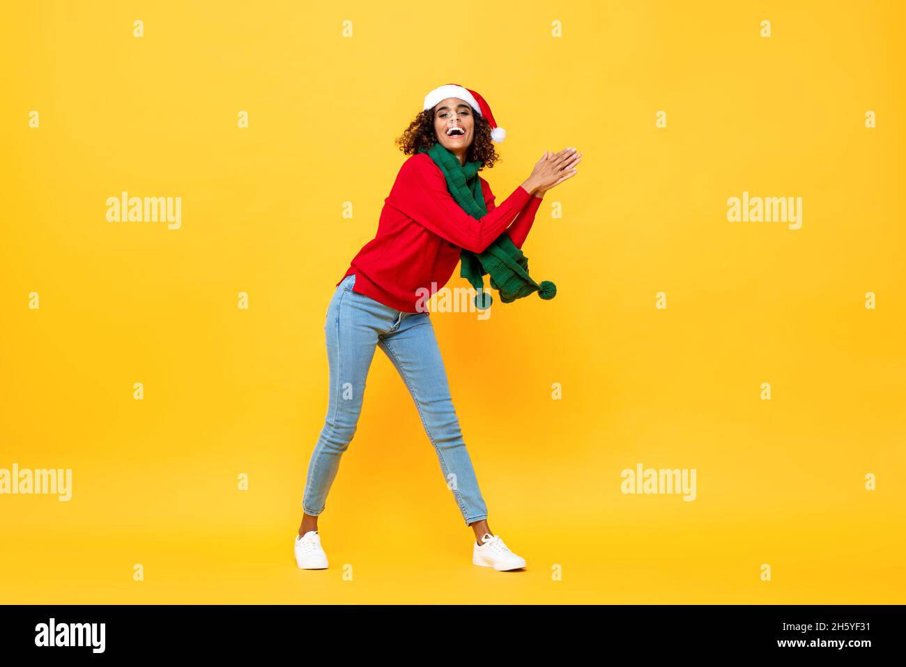 In voller Länge Porträt von Spaß glückliche Frau in Weihnachtskleidung tanzen und klatschen Hände in isolierten gelben Studio Hintergrund Stockfoto