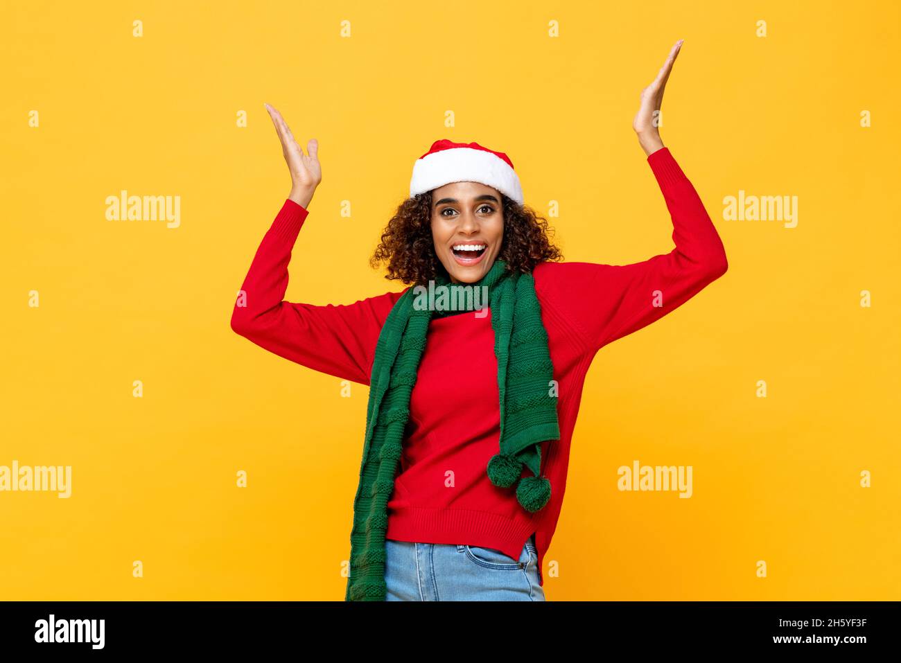 Fröhliche glückliche Frau in Weihnachtskleidung lächelnd und Hände heben Oben in gelben Studio isolierten Hintergrund Stockfoto