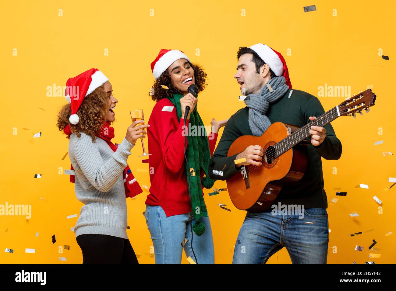 Gruppe von glücklichen verschiedenen engen Freunden mit Party singen und Weihnachten in gelben Studio Hintergrund mit Konfetti feiern Stockfoto