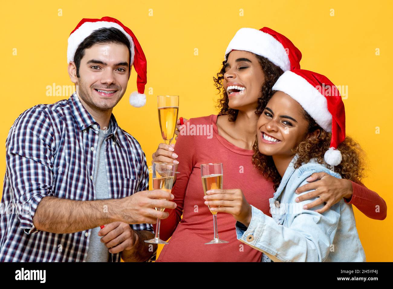 Eine Gruppe von drei verschiedenen Freunden feiert Weihnachten und trinkt gemeinsam Champagner auf gelbem Studiohintergrund Stockfoto