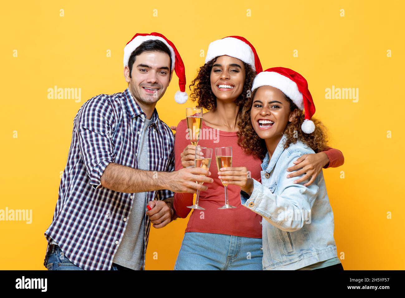 Eine Gruppe von drei begeisterten verschiedenen Freunden feiern Weihnachten trinken Champagner Zusammen auf gelbem Studiohintergrund Stockfoto