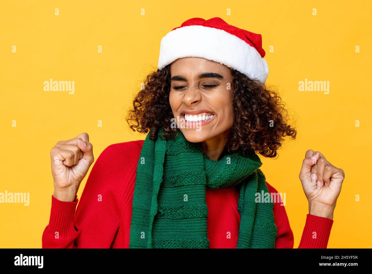 Aufgeregte Frau in Weihnachtskleidung lächelt und knallt die Hände auf einem isolierten bunten gelben Hintergrund Stockfoto