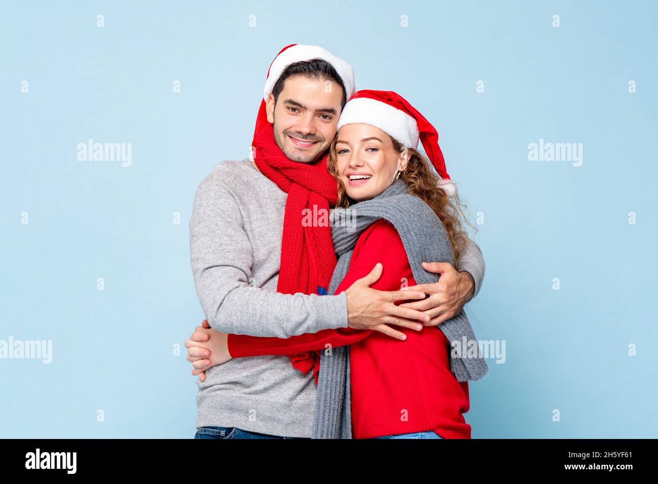 Portrait von glücklichen kaukasischen Paar in Weihnachten Outfits umarmen einander in hellblau isoliert Studio Hintergrund Stockfoto