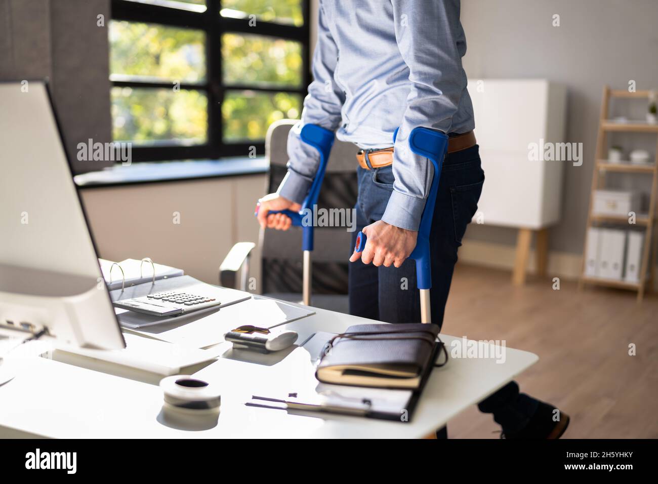 Arbeiter Mit Krücken Am Arbeitsplatz Oder Im Büro. Rehabilitationsleistungen Stockfoto