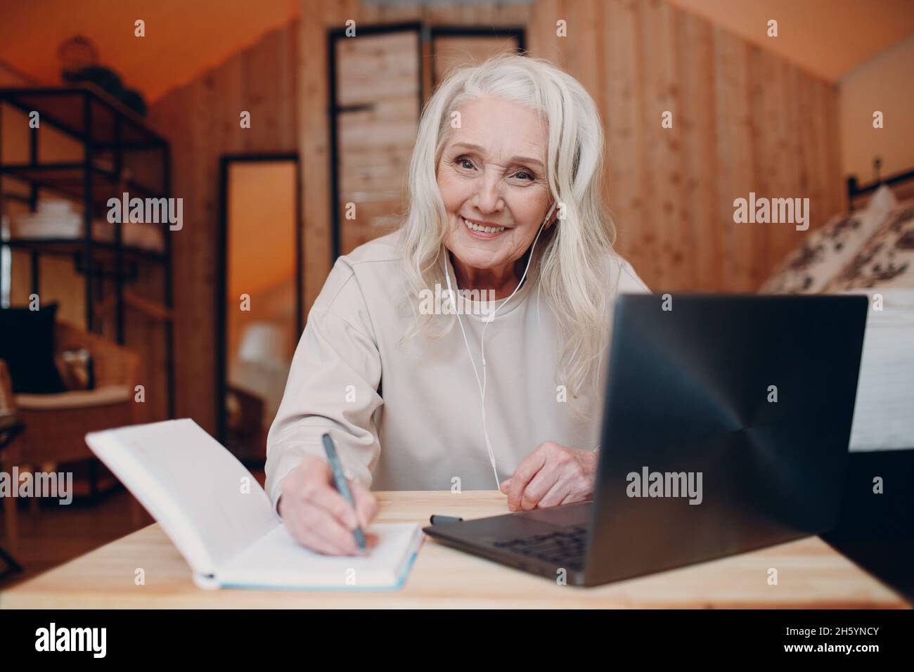 Ältere, 60-70 Jahre alte Frau mit Laptop, die am Tisch sitzt und im Glamping-Zelt spricht. Modernes Urlaubsstilkonzept Stockfoto