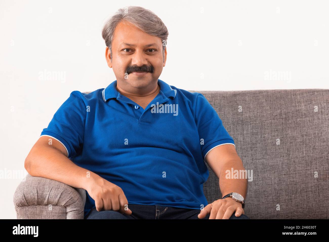 Ein indischer Mann, der mit guter Laune auf dem Sofa sitzt Stockfoto