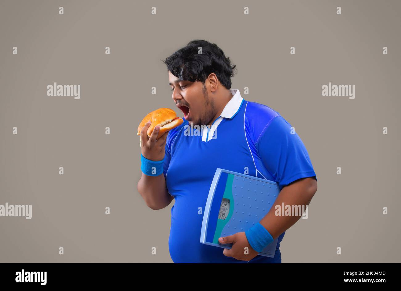 Porträt eines fetten Mannes, der eine Wiegemaschine hält und einen Burger vor dem Hintergrund des Plains isst. Stockfoto