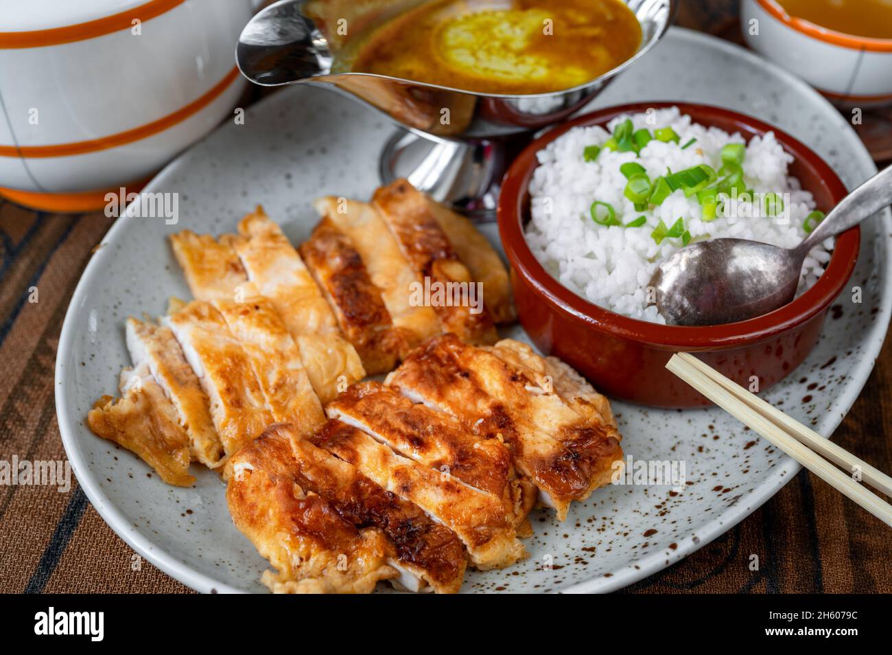 In Scheiben geschnittenes Hühnerfleisch, gebraten in knuspriger Panko-Brotkrume, Reis in der Schüssel, Chopstick, würzige Sauce in Soße Boot, Tee auf dem Tisch. Asiatisches Essen. Stockfoto