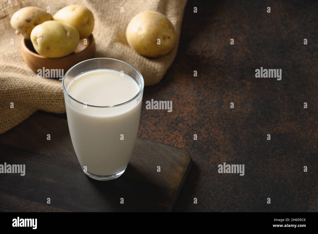 Vegane Kartoffelmilch und Kartoffel auf braunem Hintergrund. Nahaufnahme. Speicherplatz kopieren. Milchaustauschstoff auf pflanzlicher Basis und laktosefrei. Stockfoto