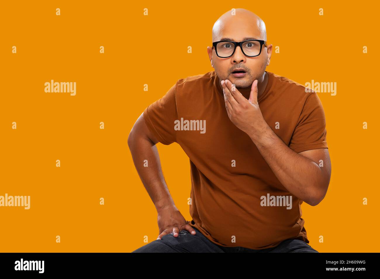 Porträt eines kahlen Mannes mit Brillen erstaunt beim Denken mit den Händen auf dem Kinn vor schlichtem Hintergrund. Stockfoto