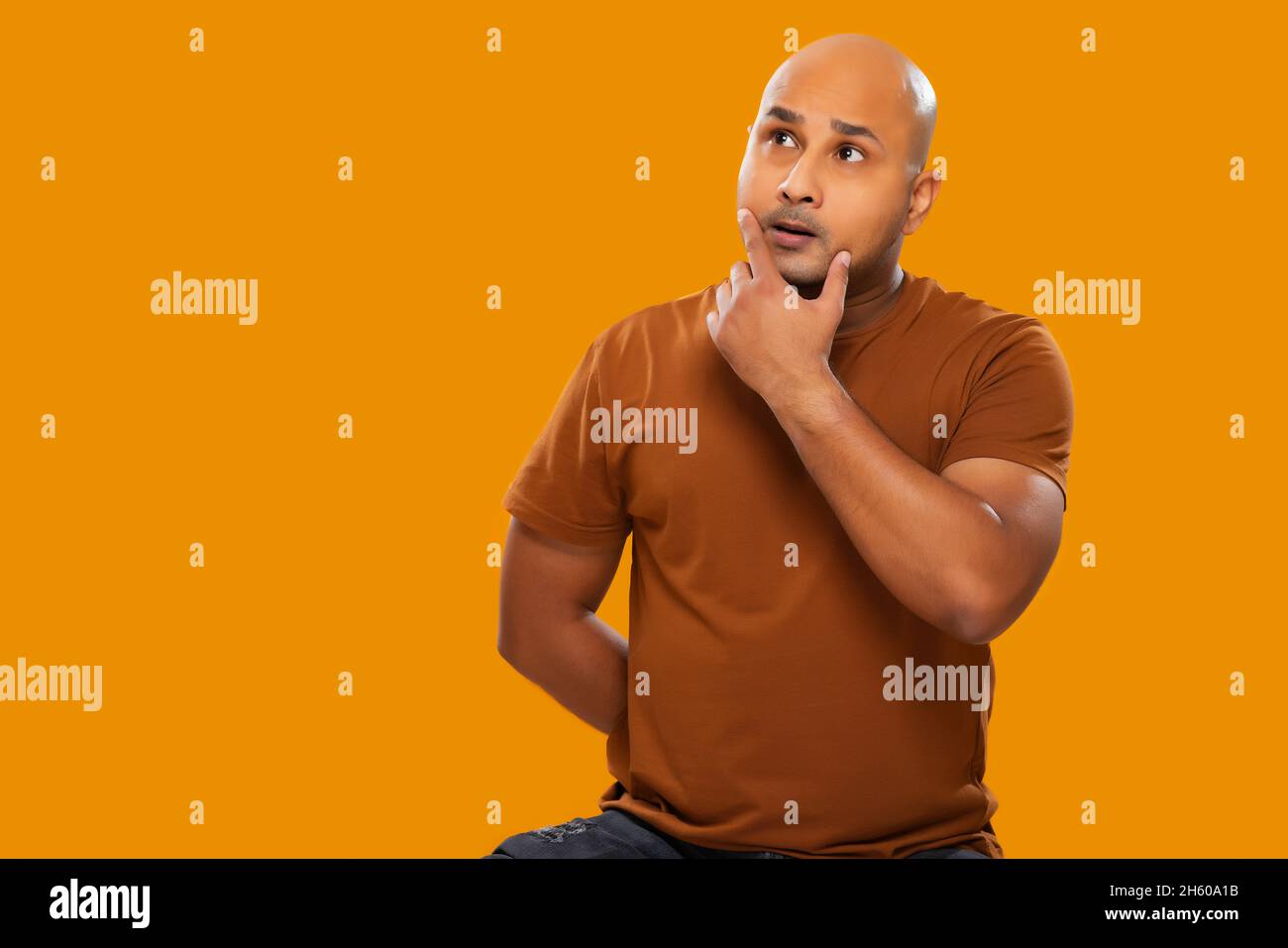 Porträt eines kahlen Mannes, der mit den Händen am Kinn vor schlichtem Hintergrund denkt. Stockfoto