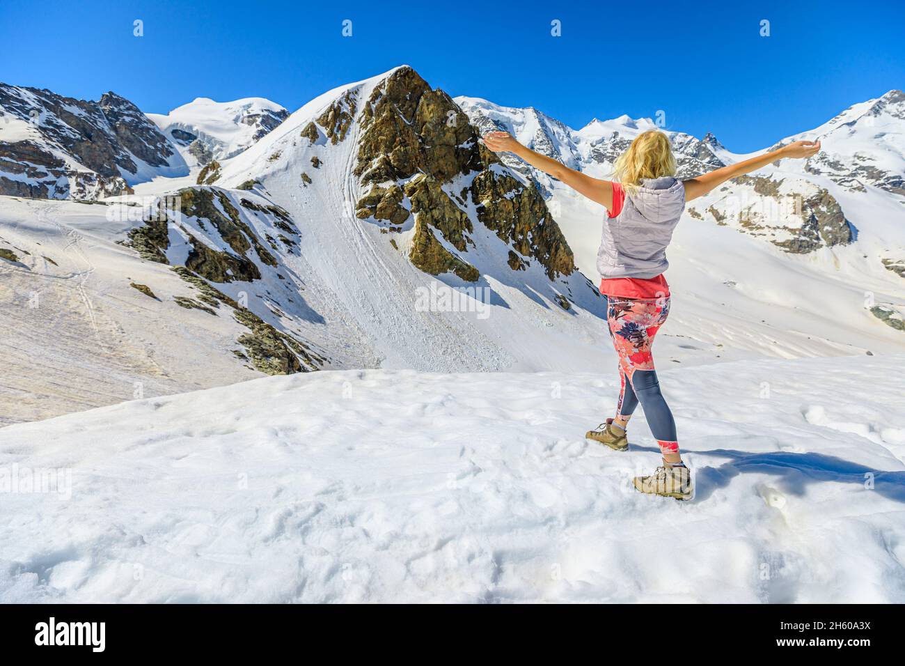 Frau mit offenen Armen, die bei Sonnenuntergang das Panorama von Diavolezza col in der Schweiz genießt. Blick auf die Skyline des Piz Bernina mit dem Morteratschgletscher in Graubünden Stockfoto