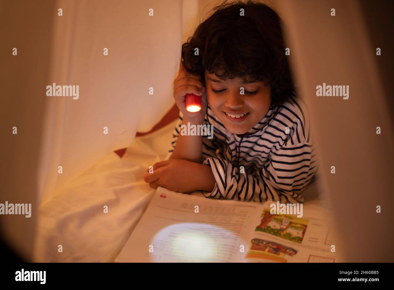 Ein Junge studiert Buch auf dem Bett mit Fackelschein Stockfoto