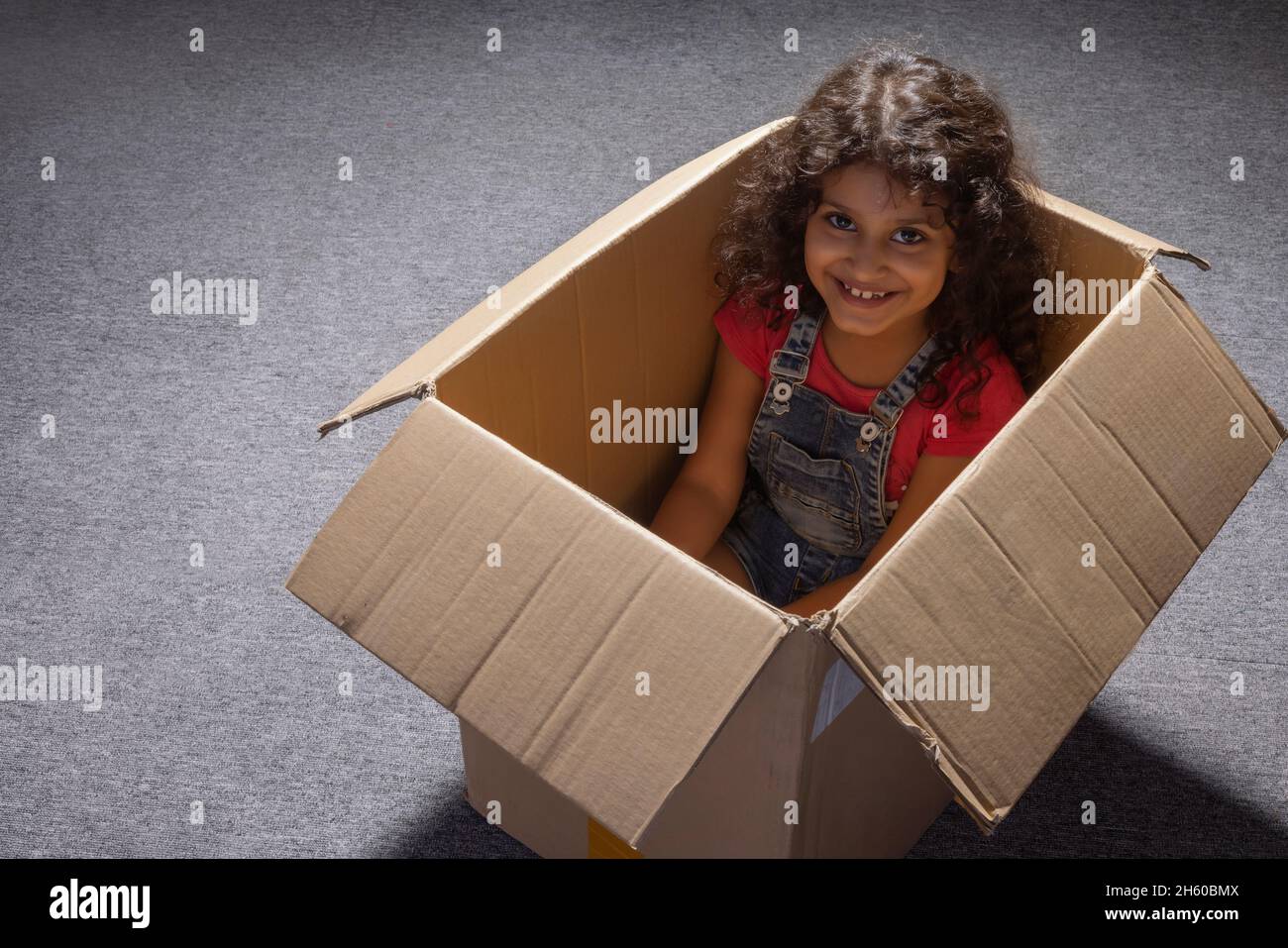 Nettes Mädchen glücklich sitzen in Box beim Spielen Stockfoto