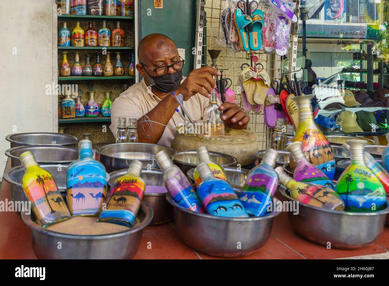 Aqaba, Jordanien - 21. Oktober 2021: Straßenszene mit einem Handwerker, der Glasflaschen mit buntem Sand in Aqaba, Jordanien, zubereitete Stockfoto