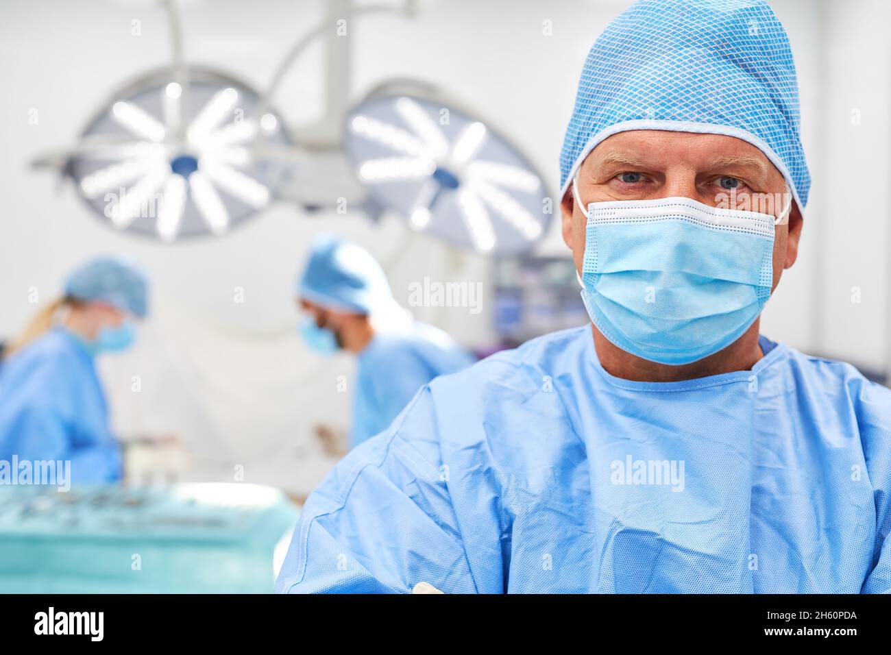 Oberarzt oder Chefarzt mit Gesichtsmaske vor seinem Team im Operationssaal Stockfoto