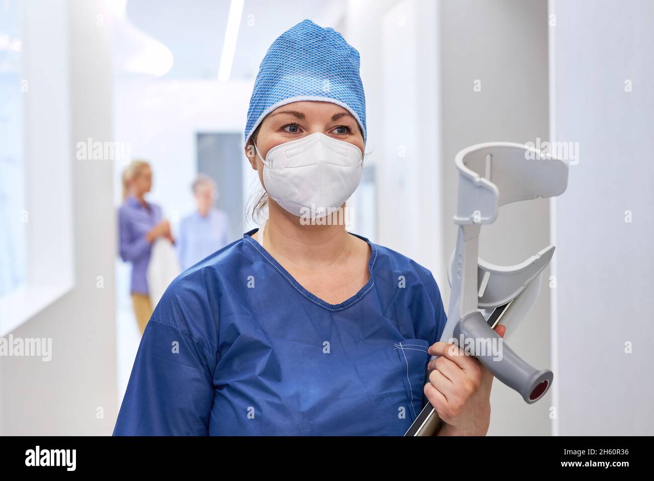 Pflegekraft oder Krankenschwester mit Gesichtsmaske und Kapuze mit Krücken in der Reha-Klinik Stockfoto